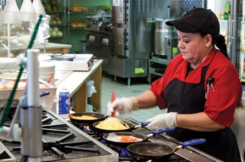 Aramark chef cooking skillets on an industrial stove.